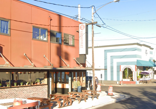 A street view of a restaurant with outdoor seating, featuring a sign that reads "Yaowarat" and nearby colorful buildings.